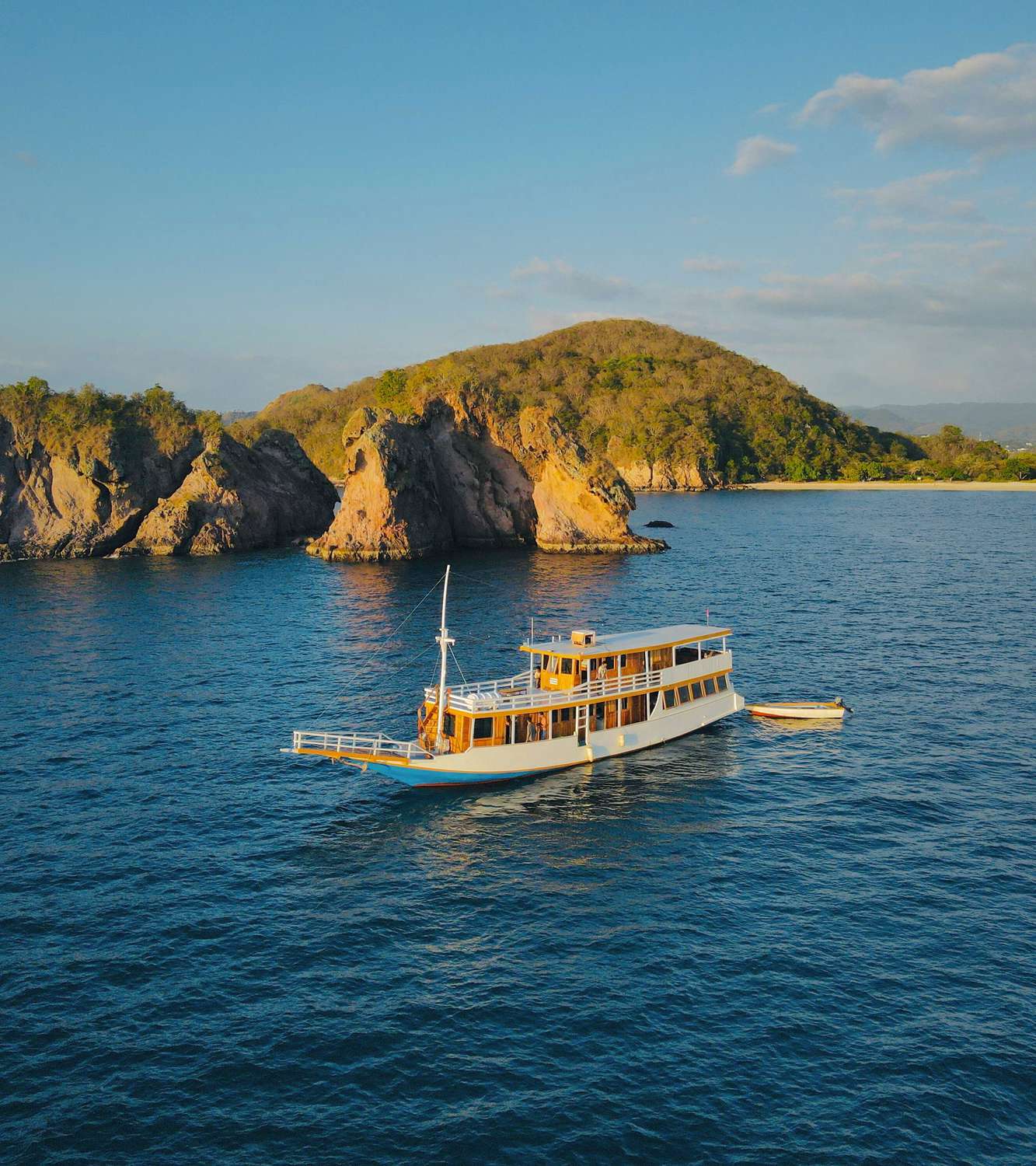 New Pandawa liveaboard boat anchored beside a green Komodo island